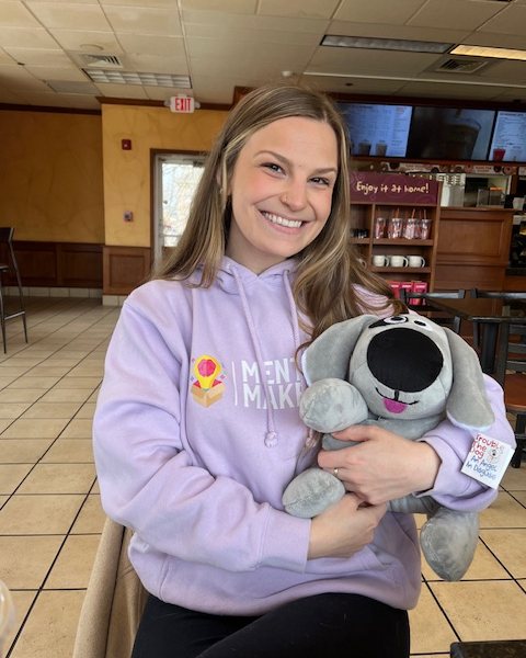 A young woman holding Trouble the Dog, wearing a mental-health awareness hoodie